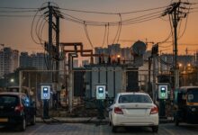 Electric vehicle charging points beside a substation transformer at dusk, with a car, a sedan and an auto-rickshaw parked nearby