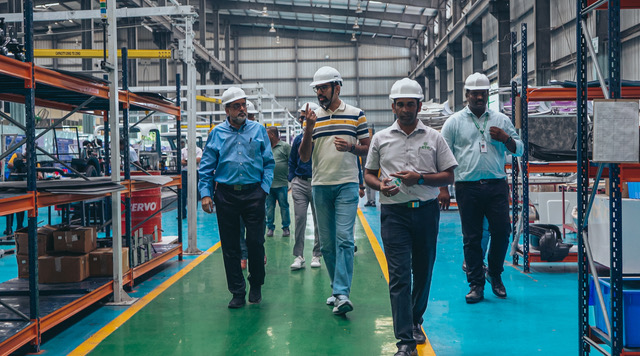 Purple electric three-wheelers moving along an assembly line in an ETO factory, with technicians in grey ETO uniforms fitting doors and components at each station