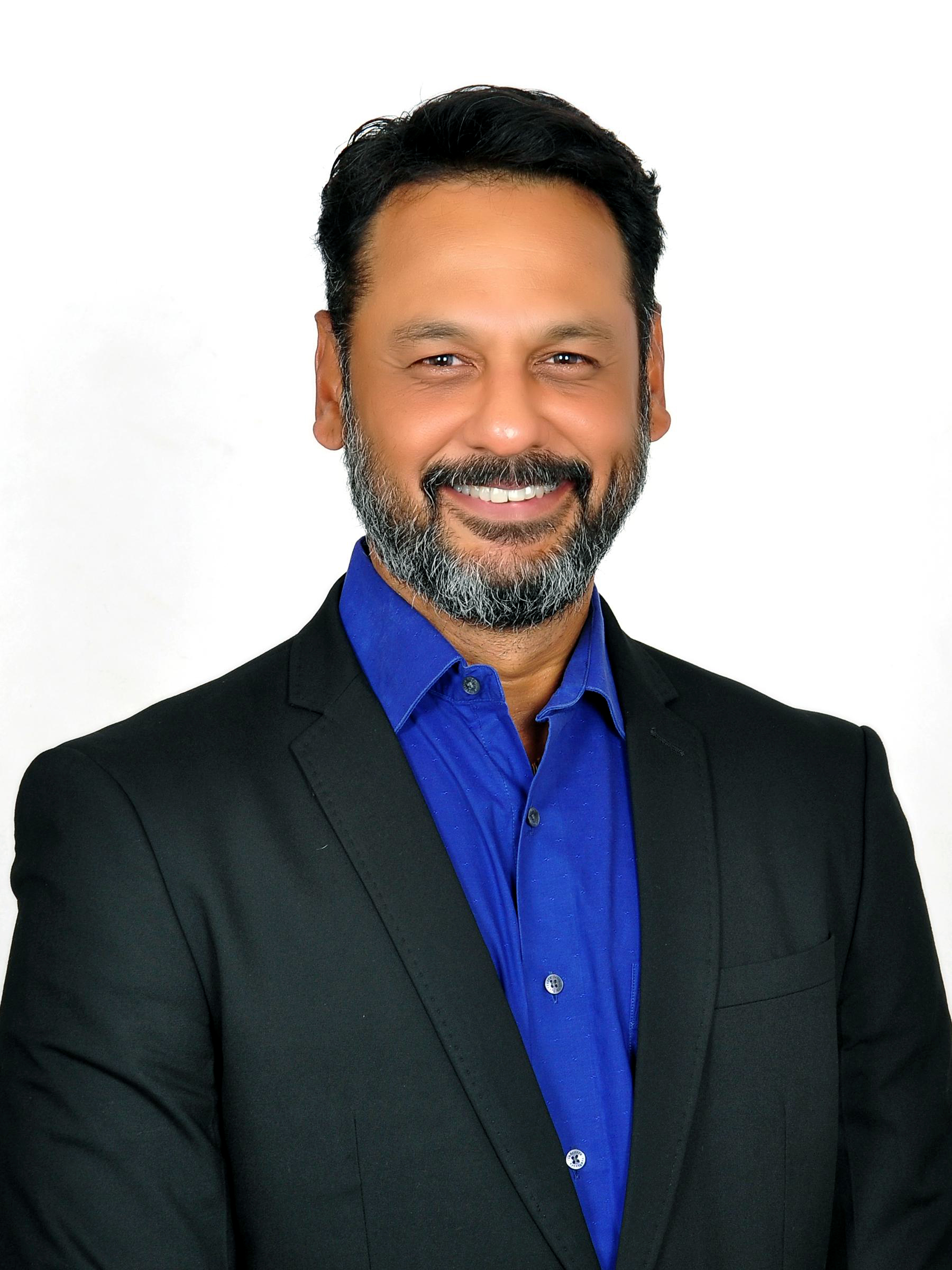Headshot of Kishore Balaji, Executive Director, GRA – IBM, India and South Asia, smiling in a black suit and bright blue shirt against a white background