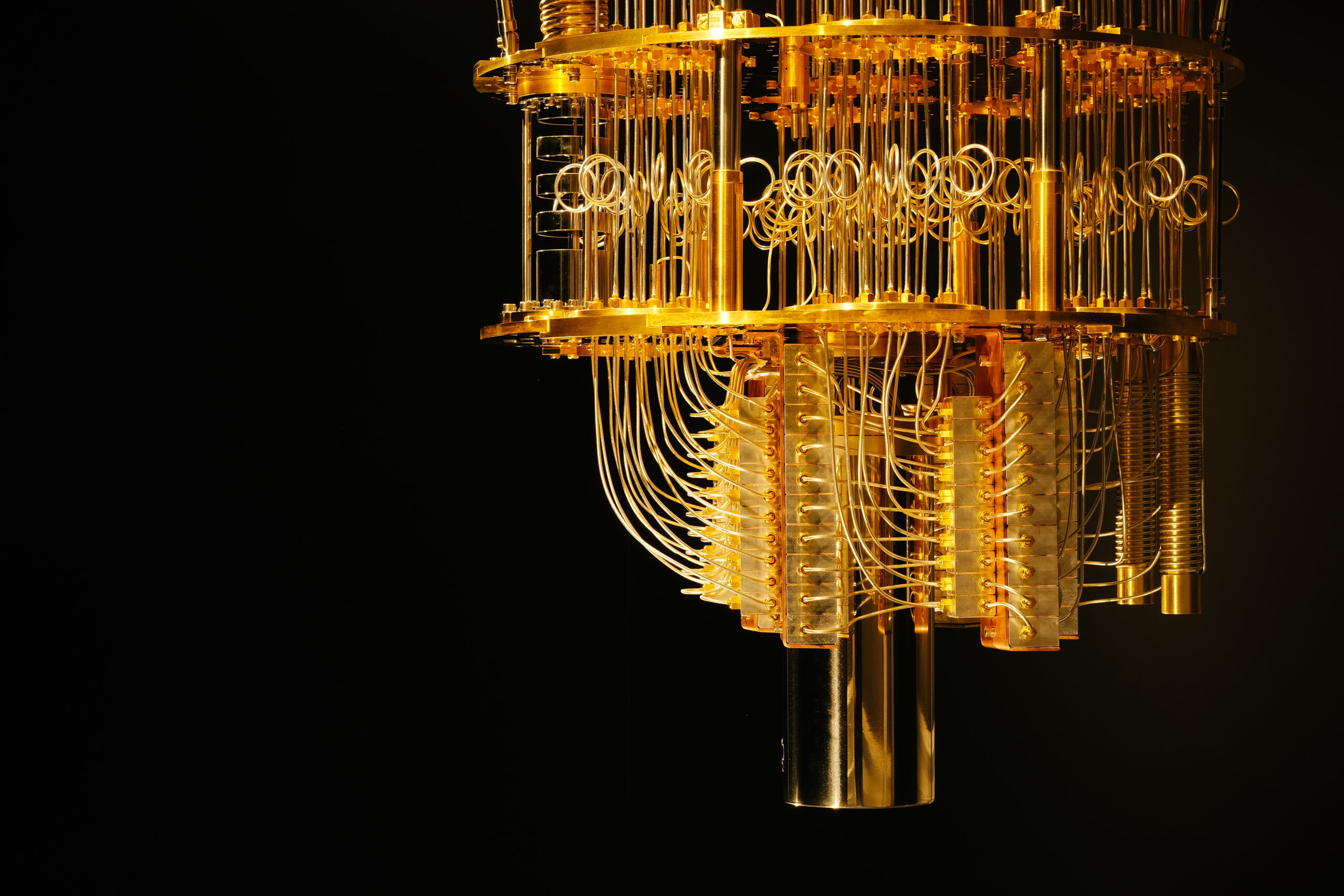 Close-up of a gold-plated quantum computer cryostat with coiled wiring and metal shielding against a black background