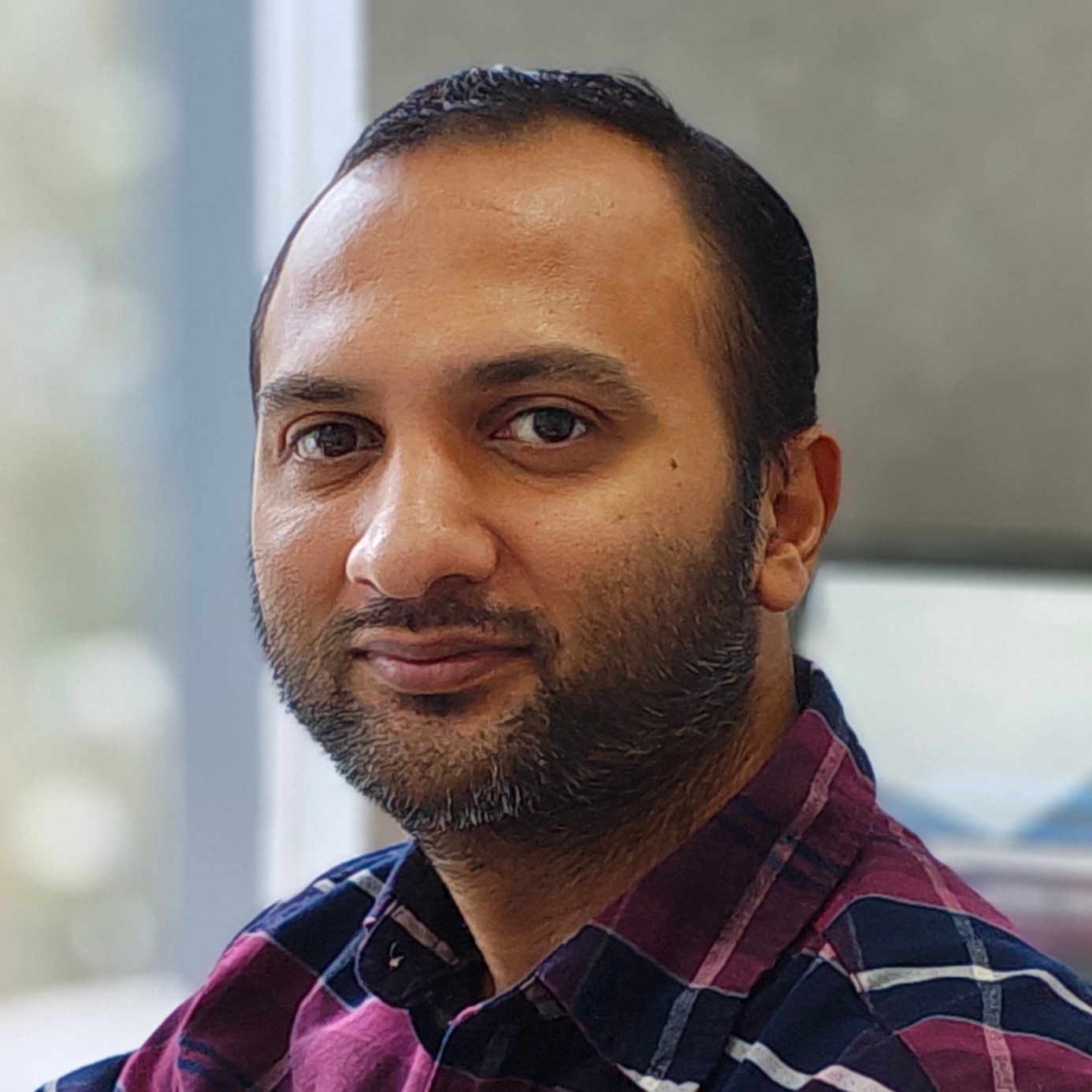 Portrait of Krishna Pratap Madathil, Head of R&D for E-Powertrain at Greaves Cotton Limited, in a blue and purple checked shirt against a blurred indoor background